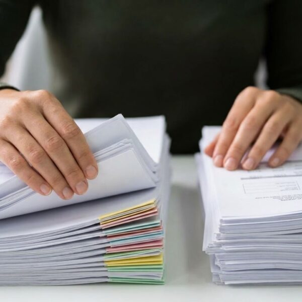 Hands sorting documents into different piles on a desk.
